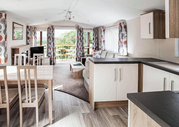Une cuisine moderne avec des meubles en bois, un coin repas avec des chaises et une vue sur l’extérieur.
