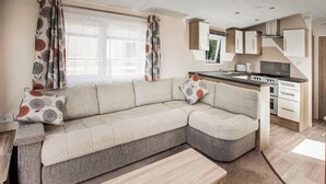 Un espace de vie moderne comprenant un canapé, une table basse, une cuisine avec un fourneau et une fenêtre avec des rideaux.