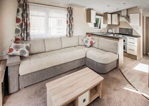 Un espacio moderno para vivir con sofá, una mesa de centro, cocina con estufa y ventana con cortinas.