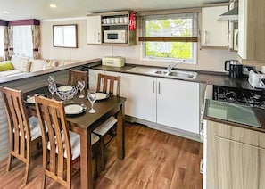 Una cocina compacta con una mesa de comedor, sillas, microondas, panificadora y un lavamanos.