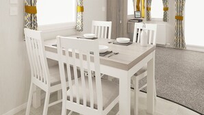 Zona pranzo con tavolo in legno, sedie bianche, termosifone bianco e tende a fantasia.