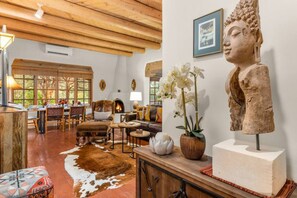 Un salon spacieux doté d’une cheminée, de poutres apparentes en bois, d’une statue de Bouddha et d’un tapis en peau de vache.
