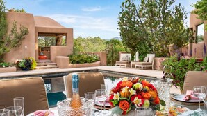 Un área de comedor al aire libre con piscina, rodeada de vegetación y arquitectura moderna.