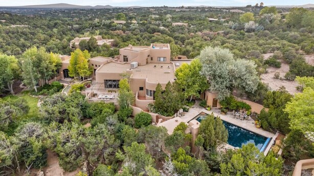 Una casa grande de varios pisos rodeada de abundante vegetación, con piscina y zona de estar al aire libre.
