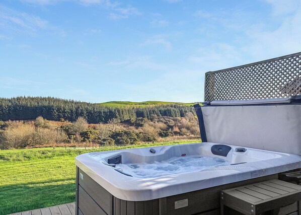 A hot tub on a deck with a view of a forested hillside.