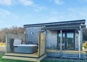 A modern wooden cabin with a hot tub, a deck, and a glass door leading to a covered patio. - This Studio Lodge is perfect for couples. (Ringford)
