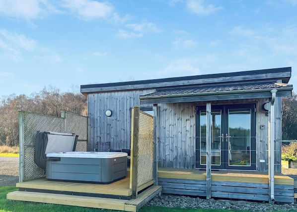 A modern wooden cabin with a hot tub, a deck, and a glass door leading to a covered patio. - This Studio Lodge is perfect for couples. (Ringford)