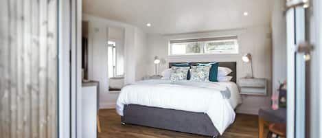 Une chambre avec un grand lit, des tables de chevet, une fenêtre et un plancher en bois.