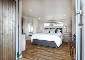 A bedroom with a large bed, bedside tables, a window, and a wooden floor. - This Studio Lodge is perfect for couples. (Ringford)