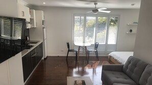 Ett kompakt bostadsutrymme med ett litet kök, en matplats, en soffa och en takfläkt.