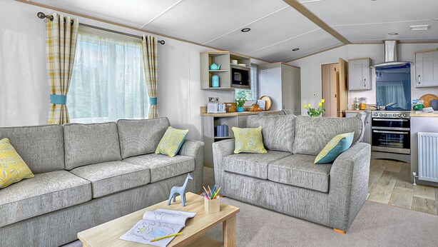 A living room with two grey sofas, a wooden coffee table, and a kitchen area with a stove and cabinets. - Thoughtfully designed for comfort and style. (Withernsea)