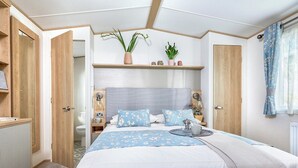 A bedroom with a bed, bedside tables, a nightstand, a window with curtains, and a door. - Thoughtfully designed for comfort and style. (Withernsea)