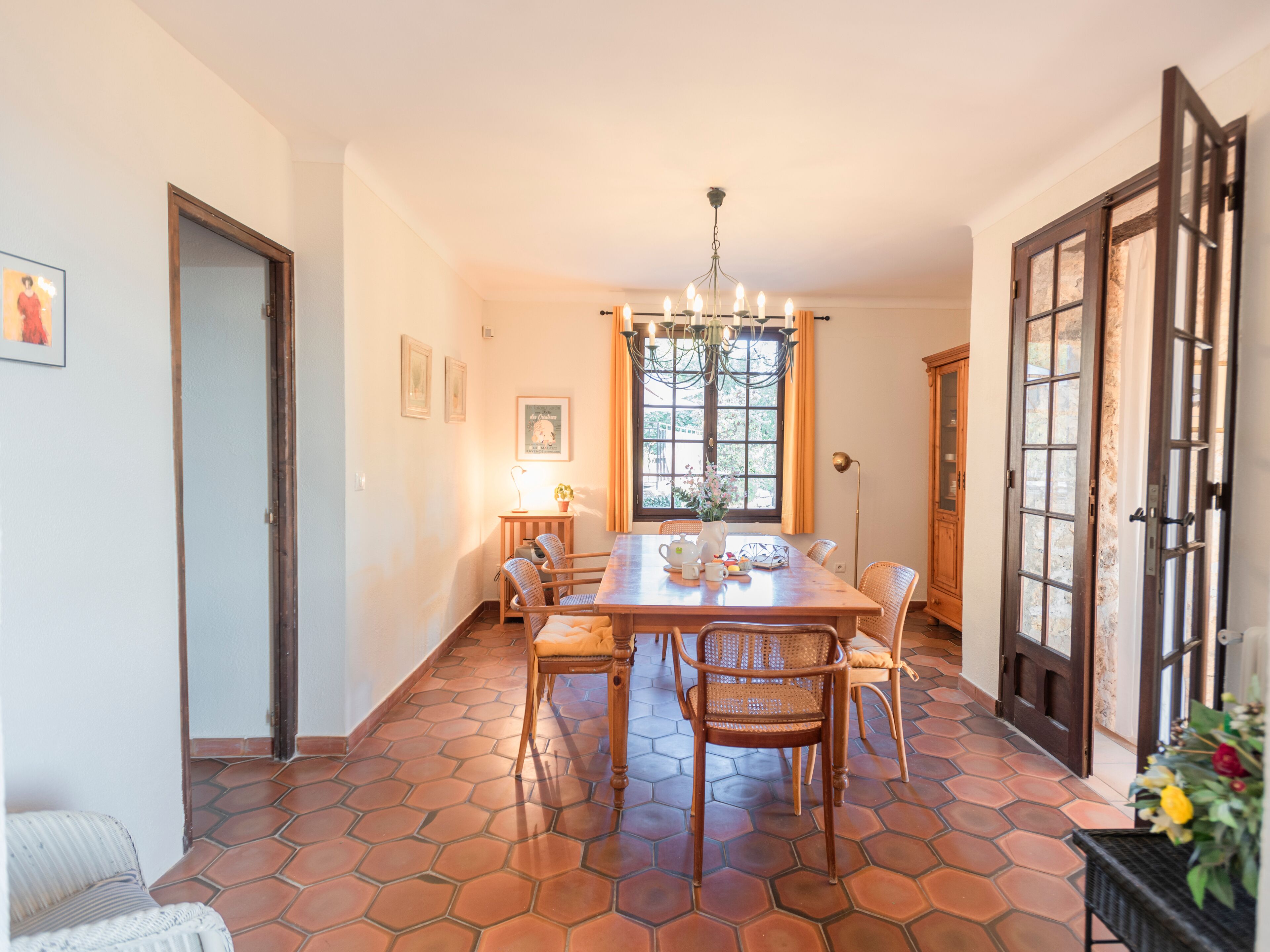 Un comedor con una mesa de madera, sillas, una araña y una ventana con cortinas.