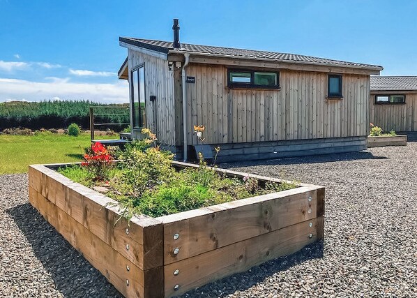 A wooden cabin with a raised garden bed, a chimney, and a gravel driveway. - This Studio Lodge is perfect for couples. (Ringford)
