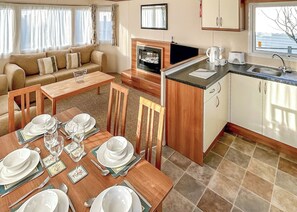 Un espacio habitable compacto con sofá, mesa de comedor para cuatro, zona de cocina con fregadero y estufa, y un televisor.