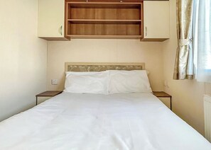 Una cama con ropa de cama blanca, cabecera de madera y repisa incorporada arriba.