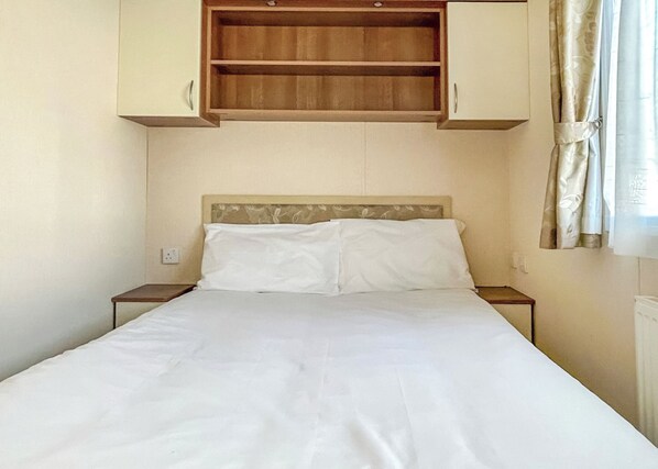 Un lit avec du linge de lit blanc, une tête de lit en bois et une étagère intégrée au-dessus.