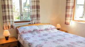 A bedroom with a floral bedspread, two bedside lamps, a wooden headboard, and a window with curtains. - 2 bedroom accommodation in Wroxham, Norfolk Broads (Wroxham, Norfolk Broads)