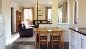A dining area with a table and chairs, a sofa, a kitchen with cabinets, and a refrigerator. - 2 bedroom accommodation in Wroxham, Norfolk Broads (Wroxham, Norfolk Broads)
