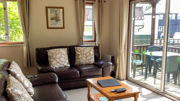 A living room with a brown leather sofa, a wooden coffee table, and a framed picture on the wall. - 2 bedroom accommodation in Wroxham, Norfolk Broads (Wroxham, Norfolk Broads)