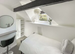 Een slaapkamer met dakraam, nachtkastje, spiegel en inloopkast.