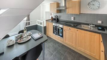 A modern kitchen with a dining area, a built-in oven, and a clock on the wall.