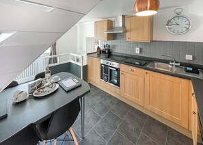 Een moderne keuken met een eethoek, een inbouwoven en een klok aan de muur.