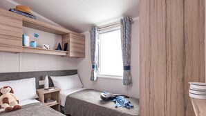 Un dormitorio con dos camas, una ventana con cortinas, una estantería con objetos personales y un armario de madera.