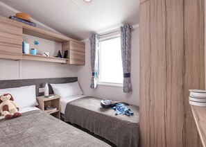 A bedroom with two beds, a window with curtains, a shelf with personal items, and a wooden wardrobe. - 3 bedroom accommodation in Newbridge, Nr Yarmouth (Newbridge, Nr Yarmouth)
