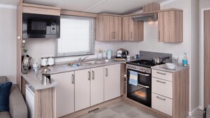 Cocina compacta con microondas, estufa, fregadero y armarios de madera.