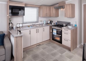 A compact kitchen with a microwave, stove, sink, and wooden cabinets. - 3 bedroom accommodation in Newbridge, Nr Yarmouth (Newbridge, Nr Yarmouth)