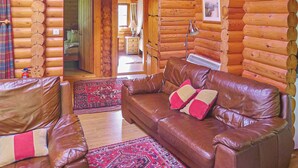 A log cabin interior with a leather sofa, a patterned rug, and a wooden wall. - 2 bedroom accommodation in Craobh Haven, Argyll (Craobh Haven, Argyll)