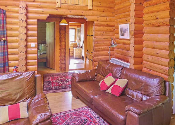 A log cabin interior with a leather sofa, a patterned rug, and a wooden wall.