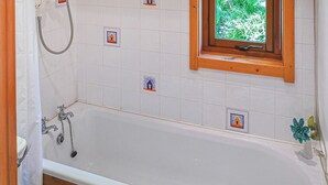 A bathroom with a bathtub, a window with a view of greenery, and a shower. - 2 bedroom accommodation in Craobh Haven, Argyll (Craobh Haven, Argyll)