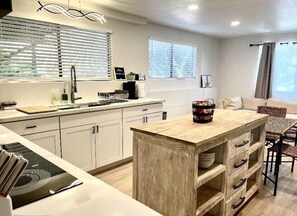 A modern kitchen with white cabinetry, a wooden island, and a dining area with a woven chair.