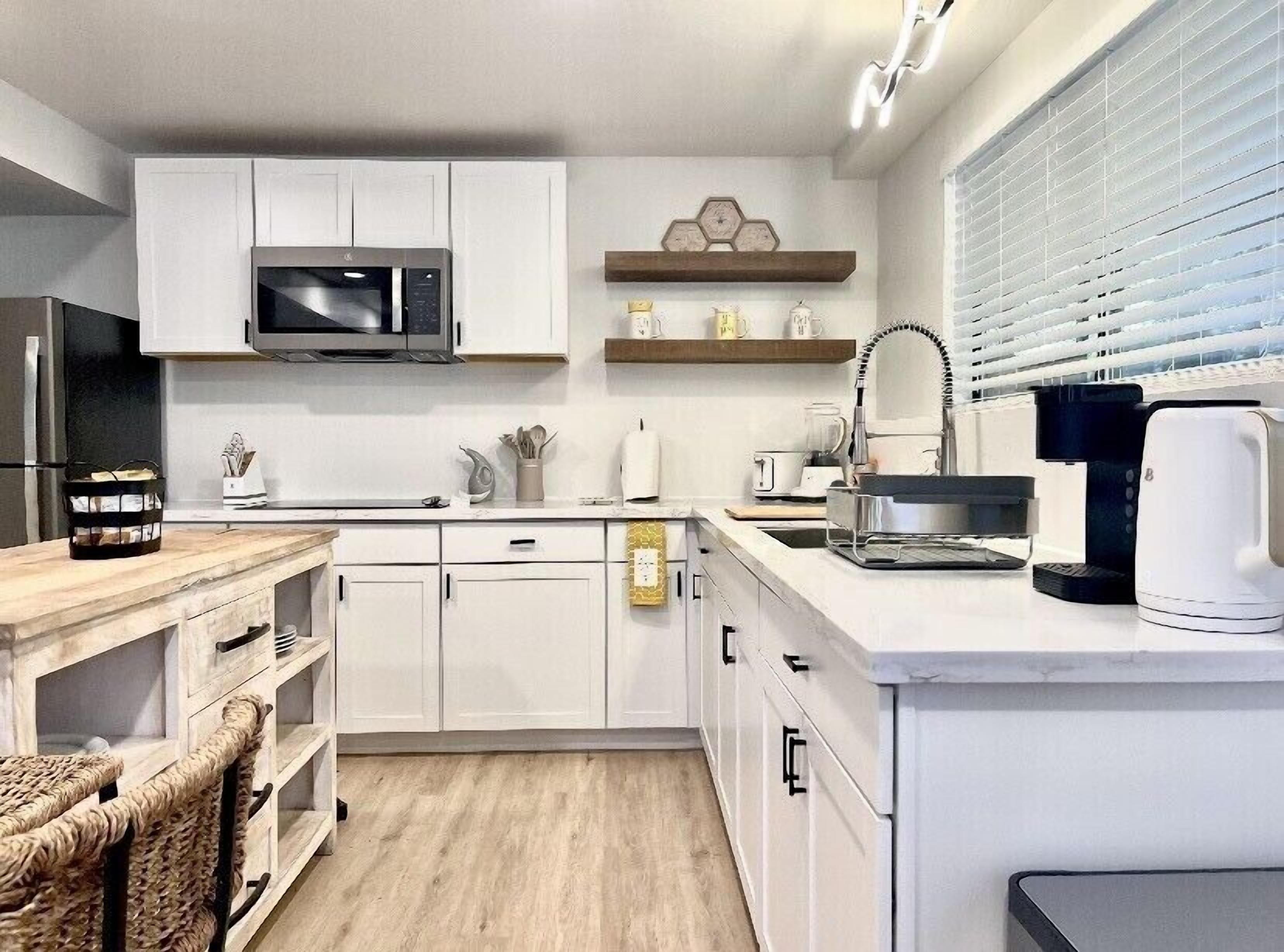Una cocina moderna con armarios blancos, microondas, cafetera y horno empotrado.