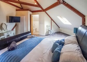 Un dormitorio con techo inclinado, cama, escritorio, silla y televisor.