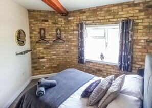Une chambre avec un mur en briques, une fenêtre avec des rideaux, un lit avec des oreillers et un miroir.