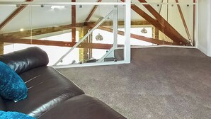 Una habitación con un sofá de cuero marrón, alfombra gris y vistas a una escalera de madera.