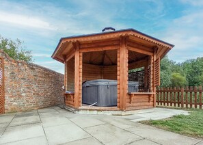 A wooden gazebo with a hot tub, brick wall, and wooden fence.