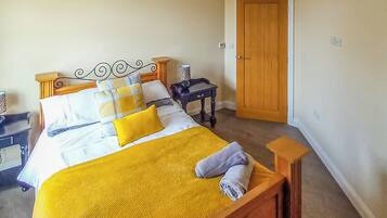 A neatly made bed with a yellow blanket, a wooden headboard, and a small bedside table with a lamp.
