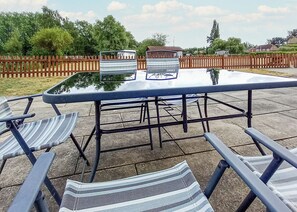 Un patio al aire libre con una mesa de vidrio, sillas de metal y una valla de madera de fondo.