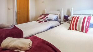 Habitación de hotel con dos camas, cada una con cabecero blanco, almohadas a rayas rojas y blancas y una manta roja.