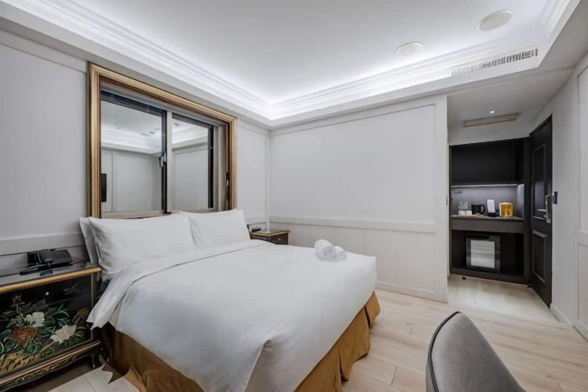 Una habitación de hotel con cama, mesita de noche, espejo y un pequeño escritorio con silla.