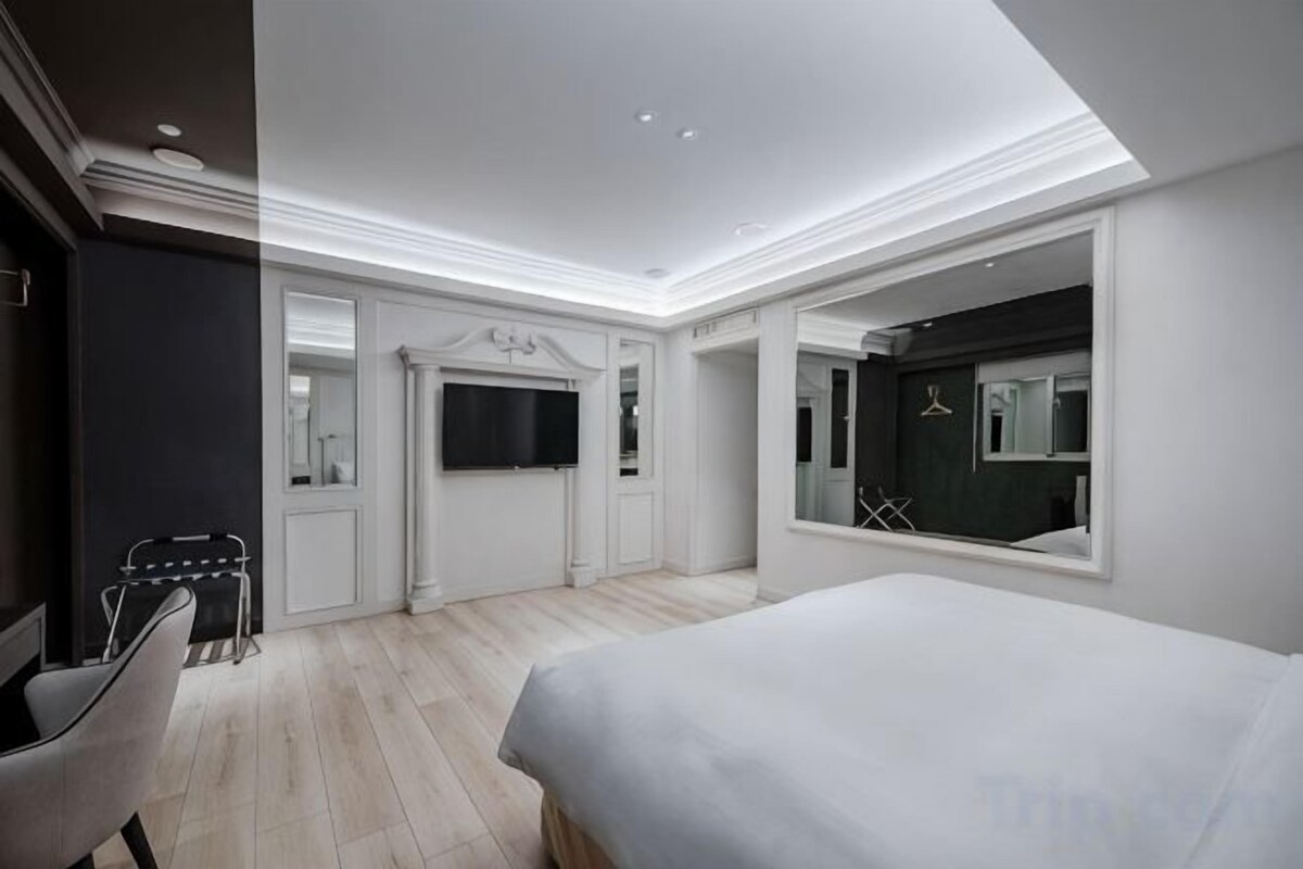 Une chambre d’hôtel moderne dotée d’un grand lit, d’un téléviseur à écran plat, d’un miroir et d’un coin salon avec une chaise et une petite table.