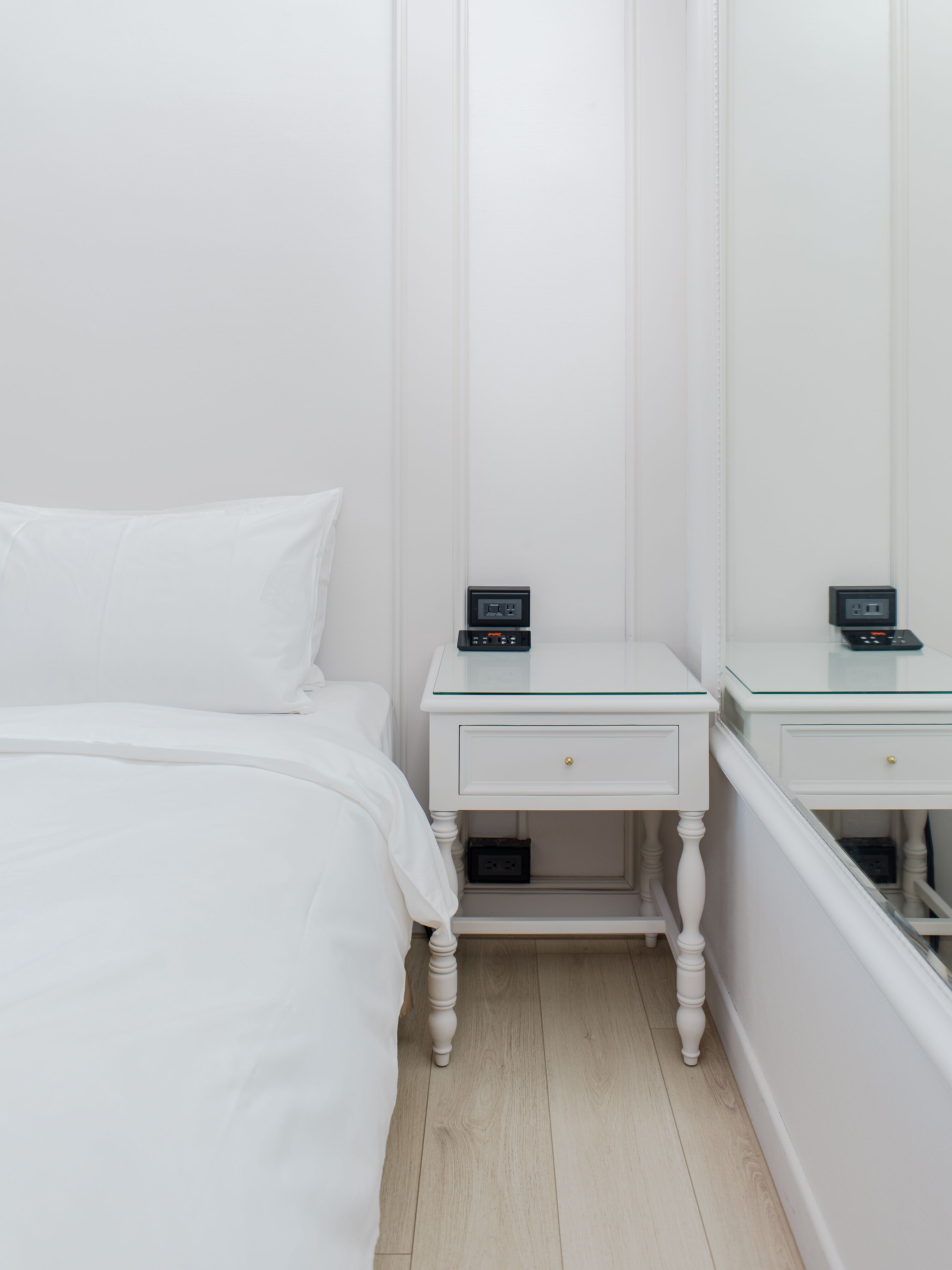 A white bedroom with a bed, two bedside tables with black power strips, and a mirror on the wall.