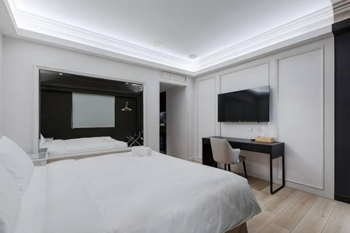 Una habitación de hotel moderna con una cama grande, un escritorio, televisión y vestidor.