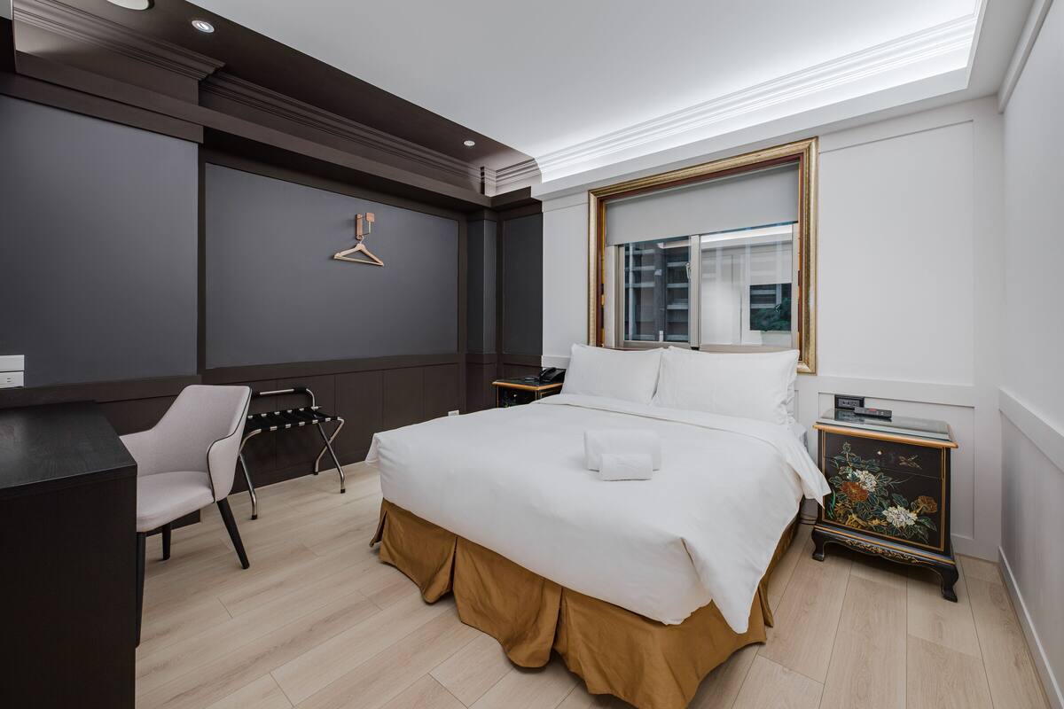 Una habitación de hotel moderna con una cama grande, un escritorio, una silla y una mesita de noche.