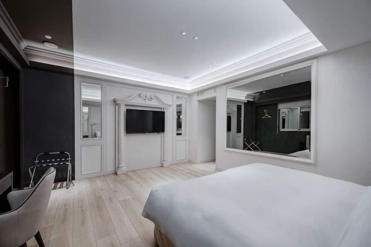 Una habitación de hotel moderna con una cama grande, televisión, espejo y zona de estar.