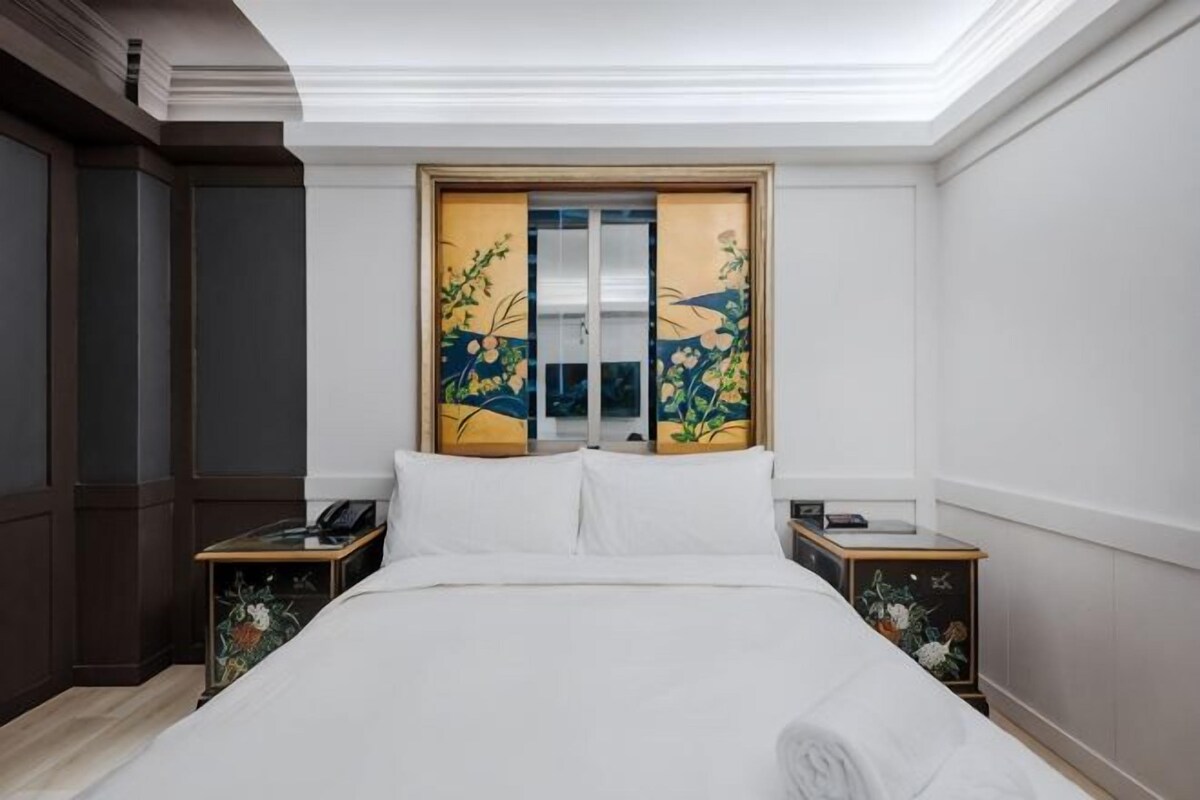 A hotel room with a bed, a nightstand, a wooden door with a floral design, and a white ceiling.
